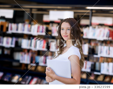 Happy female student holding books at the library Happy female student holding books at the library 33623599