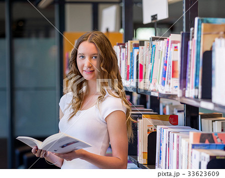 Happy female student holding books at the library 33623609