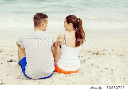 Young couple looking at each other while sitting on beach 33630705
