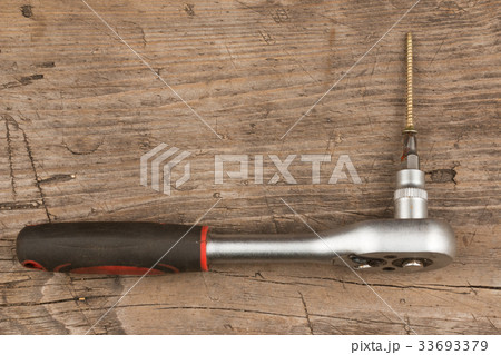 Screwdriver and screw on wooden board. 33693379