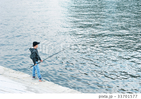 a lone boy stands on a pier with a fishing rod a lone boy stands on a pier with a fishing rod 33701577