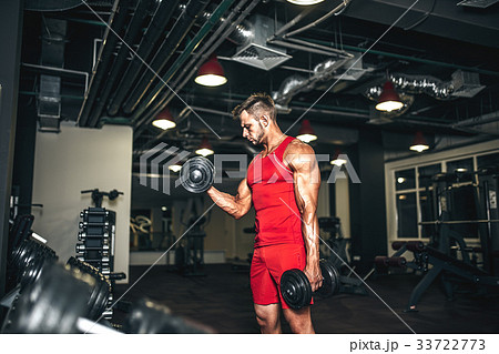 Bodybuilder lifting heavy black dumbbells at the 33722773