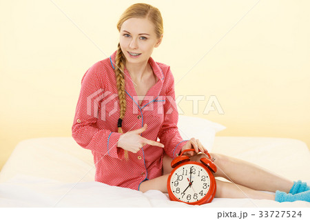 Sleepy woman wearing pajamas holding clock Sleepy woman wearing pajamas holding clock 33727524