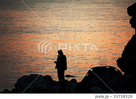 Silhouette of trekker on rocky seashore near camping tent on ove Silhouette of trekker on rocky seashore near camping tent on ove 33738526