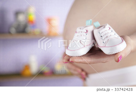 Pregnant woman holding a pair of tiny shoes 33742428