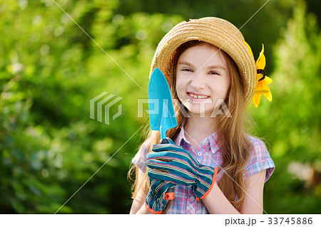 Adorable little girl wearing straw hat holding garden tools Adorable little girl wearing straw hat holding garden tools 33745886