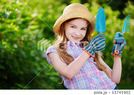 Adorable little girl wearing straw hat holding garden tools 33745902