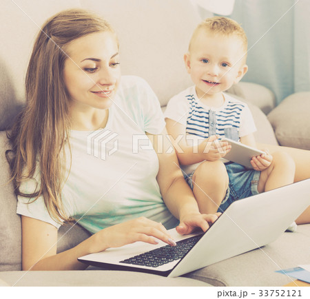 Smiling mother is productively working behind laptop while child playing on tablet 33752121