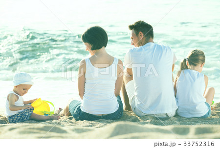 back view on family of four sitting on beach 33752316
