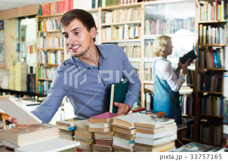 Smiling man choosing new book from many 33757165