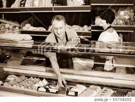 staff offering fresh baguettes and buns in bakery 33758202