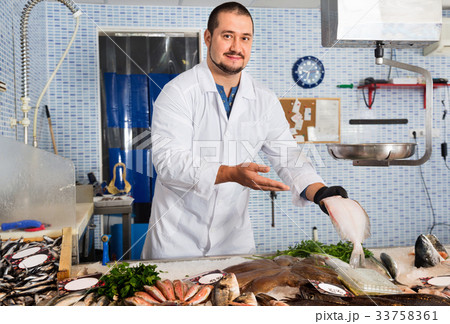 Man in glove behind counter shows fish in his hand Man in glove behind counter shows fish in his hand 33758361