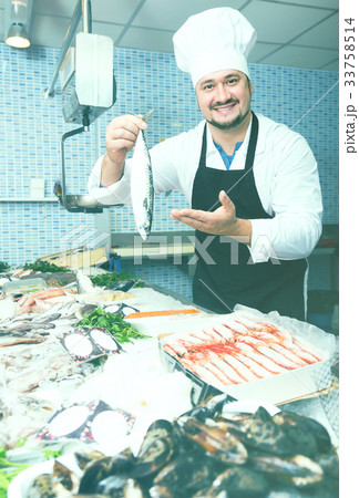 Cheerful seller shows hands fish on counter Cheerful seller shows hands fish on counter 33758514