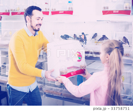 man seller demonstrating canary bird in cage to girl in pet shop 33758751