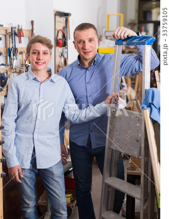 Portrait of adult father and son with stair in workshop. Portrait of adult father and son with stair in workshop. 33759105