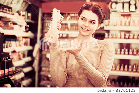 Young female shop assistant is demonstrating samples of nail polishes Young female shop assistant is demonstrating samples of nail polishes 33761125
