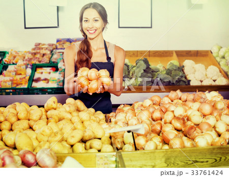 Smiling young woman seller showing yellow onions Smiling young woman seller showing yellow onions 33761424