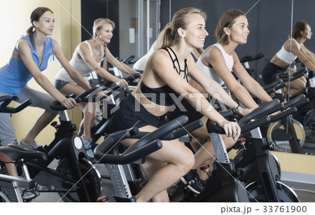 Girls during workout on stationary bicycle in fitness gym Girls during workout on stationary bicycle in fitness gym 33761900