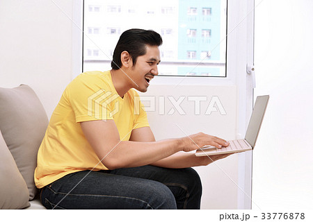 Happy asian man with laptop sitting on the couch 33776878