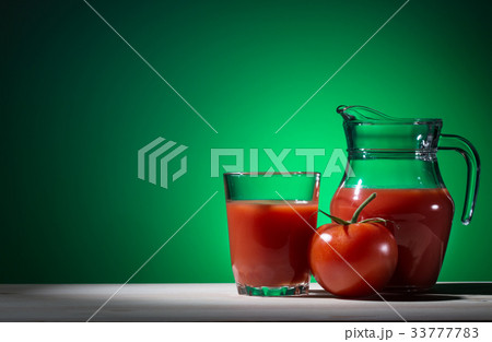 Tomato, glass and jug of tomato juice on green 33777783