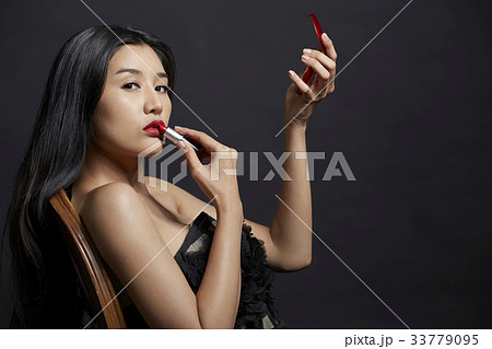 portrait of woman applying lipstick and looking at camera portrait of woman applying lipstick and looking at camera 33779095