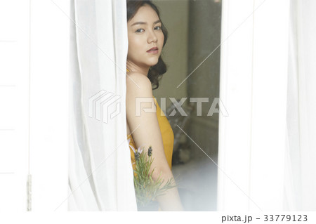 A Thai girl is standing in her room and looking outside 33779123