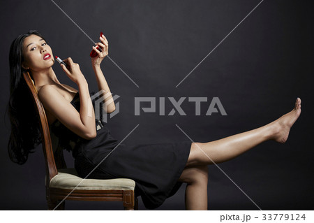 An Asian girl with a long black hair is sitting and making up on black background 33779124