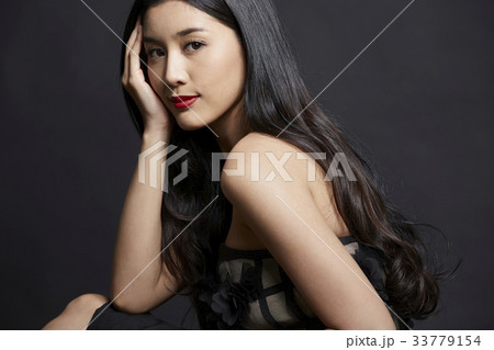 A Thai girl is sitting and touching her face with long black hair on black background 33779154