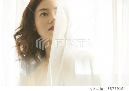 A beautiful Thai girl is standing and looking at something beside the white curtain 33779164