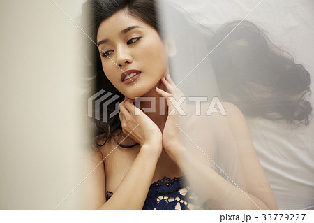portrait of a girl with a long hair lying on a bed and touching her neck 33779227