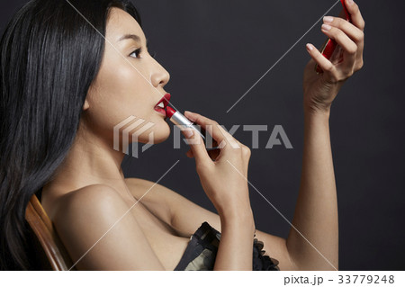 An elegant woman is leaning on the chair and looking at the hand mirror. 33779248