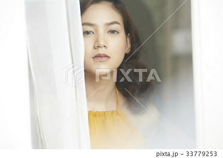 An Asian young woman standing beside the curtain and looking at camera. An Asian young woman standing beside the curtain and looking at camera. 33779253