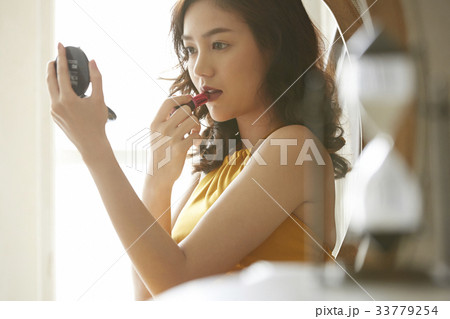 portrait of an Asian young woman using her lipstick while looking at the hand mirror. portrait of an Asian young woman using her lipstick while looking at the hand mirror. 33779254