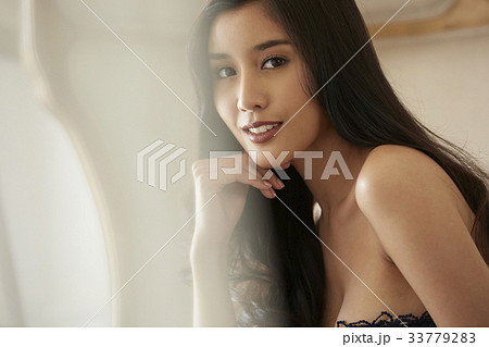An elegant lady is smiling behind the curtain inside. An elegant lady is smiling behind the curtain inside. 33779283