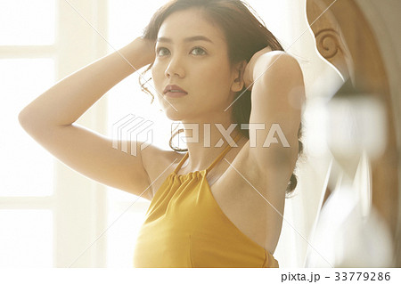 An Asian young woman is touching her hair and looking at something 33779286