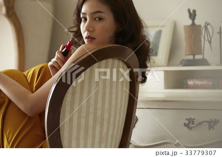 photo of a woman sitting on a chair and holding a lipstick. 33779307