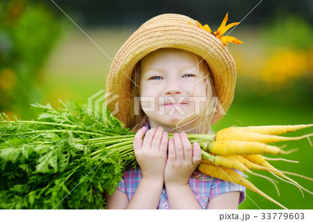 Cute little girl wearing straw hat holding a bunch of fresh organic carrots Cute little girl wearing straw hat holding a bunch of fresh organic carrots 33779603