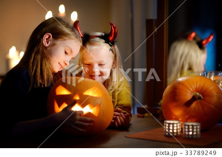 Two pretty young sisters in halloween costumes carving a pumpkin together Two pretty young sisters in halloween costumes carving a pumpkin together 33789249