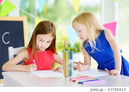 Two cute little sisters drawing with colorful pencils at a daycare Two cute little sisters drawing with colorful pencils at a daycare 33790913