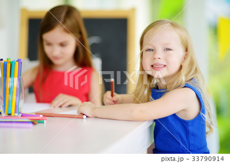 Two cute little sisters drawing with colorful pencils at a daycare 33790914