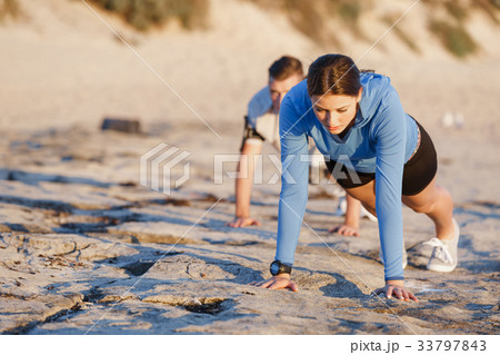 Young couple doing push ups on ocean beach 33797843