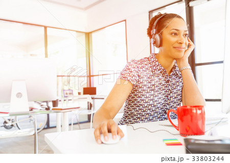 Portrait of smiling afro-american office worker sitting in offfice with headphones Portrait of smiling afro-american office worker sitting in offfice with headphones 33803244