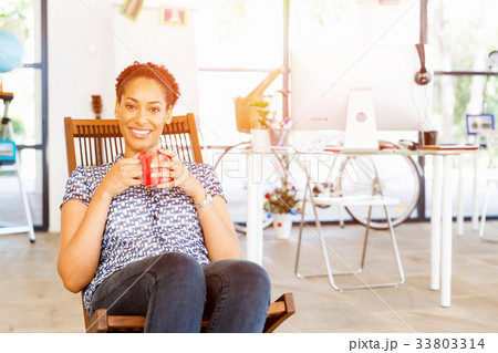 Portrait of smiling afro-american office worker sitting in offfice with mug 33803314