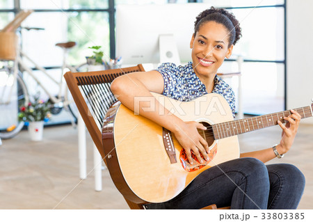 Portrait of smiling afro-american office worker sitting in offfice with guitar 33803385