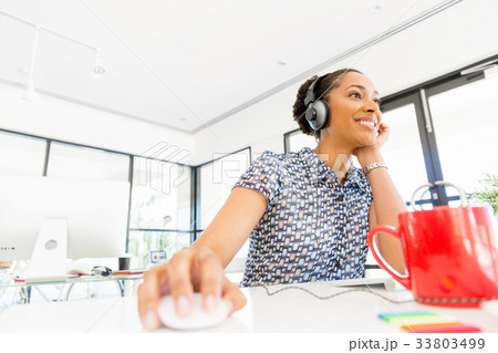Portrait of smiling afro-american office worker sitting in offfice with headphones 33803499