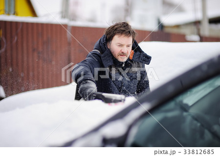 Man using tool for cleaning his car from snow 33812685