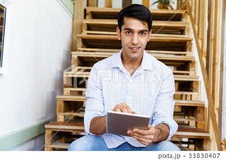 Portrait of young man sitting at the stairs in office Portrait of young man sitting at the stairs in office 33830407