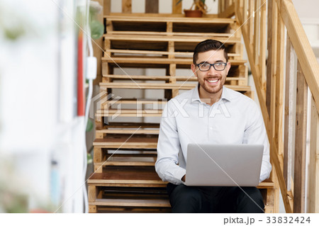Portrait of young man sitting at the stairs in office 33832424
