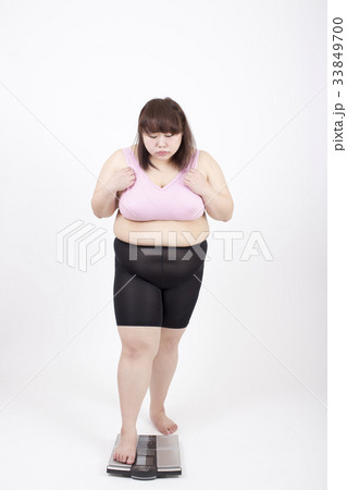 白い背景の前でそーっと体重計に乗ろうとする太った若い女性 33849700