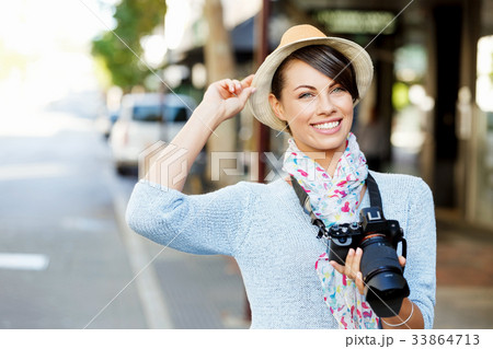 Outdoor summer smiling lifestyle portrait of pretty young woman with camera 33864713